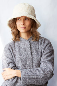 Woman wearing a textured gray sweater and cream bucket hat against a light background