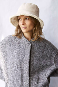 Woman wearing a textured gray sweater and beige bucket hat against a white background