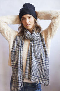 Person wearing a black knit beanie and plaid scarf against a white background