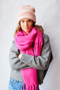 Woman wearing a pink scarf, gray sweater, and striped beanie against a white background