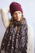 Woman wearing a leopard print scarf and maroon beanie against a white background