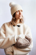 Woman wearing a cream coat, beanie, and gloves against a white background