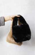 Hand holding two faux fur bags against a white background