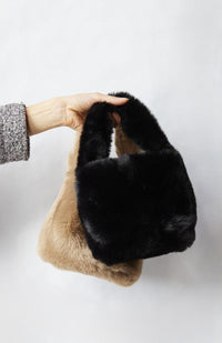 Hand holding two faux fur bags against a white background