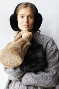 Woman wearing a gray coat and black earmuffs with a white background