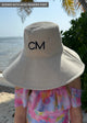 Tan packable sun hat with embroidered letters on model at the beach