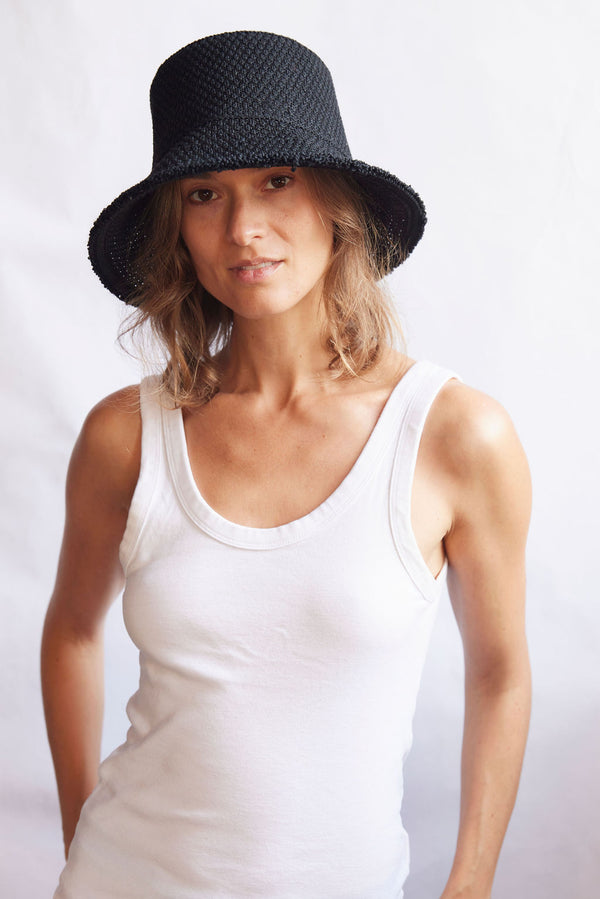 Woman wearing a black woven bucket hat and white tank top against a white background