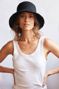 Woman wearing a black woven bucket hat and white tank top against a plain background