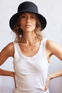 Woman wearing a black woven bucket hat and white tank top against a plain background