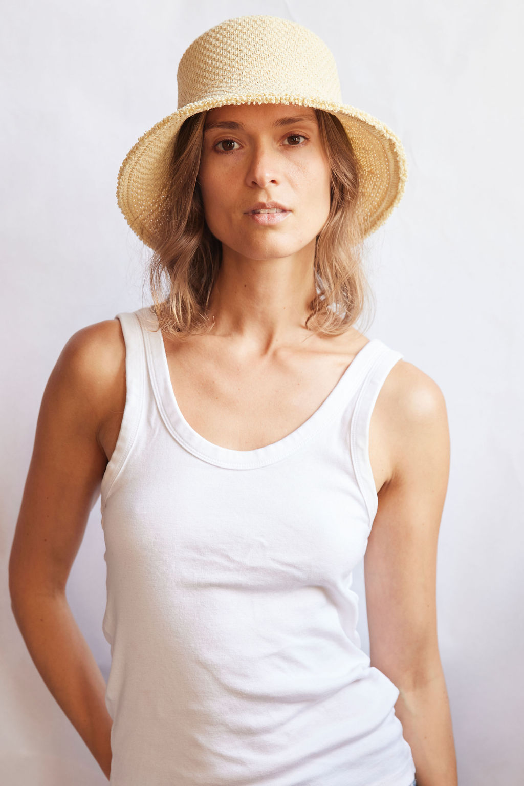 Woman wearing a woven bucket hat and white tank top against a plain background