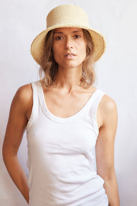 Woman wearing a woven bucket hat and white tank top against a plain background