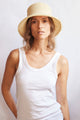 Woman wearing a woven bucket hat and white tank top against a plain background