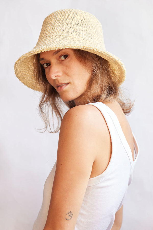 Woman wearing a woven bucket hat and white tank top against a plain background