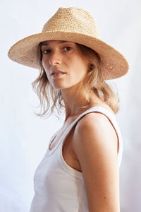 Woman wearing a straw hat and white tank top against a light background