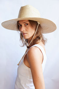 Woman wearing a wide-brimmed straw hat against a light background
