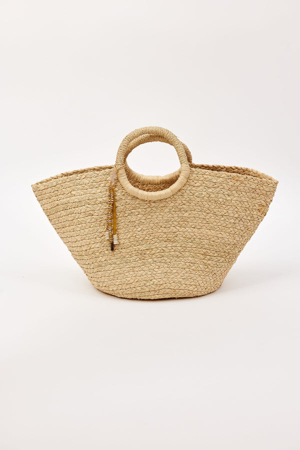 Woven straw bag with circular handles and tassel detail on a white background