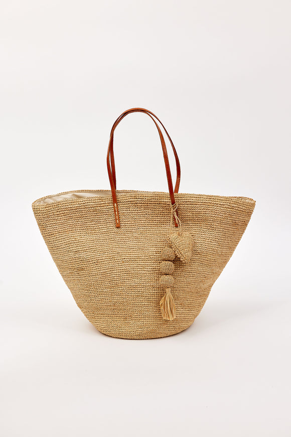 Woven straw bag with brown leather handles and a tassel detail on a white background