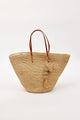 Woven straw bag with brown leather handles and a tassel detail on a white background