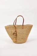 Woven straw bag with leather handle and tassel on a white background