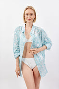 Woman wearing a light blue floral shirt over a white bikini on a white background