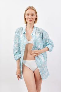 Woman wearing a light blue floral shirt over a white bikini on a white background