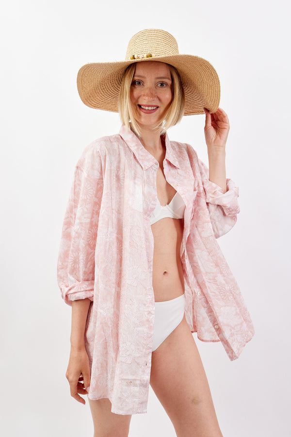 Woman wearing a pink floral cover-up and white bikini with a straw hat on a white background