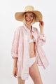 Woman wearing a pink floral cover-up and white bikini with a straw hat on a white background