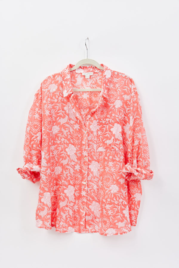 Coral floral blouse on a hanger against a white background
