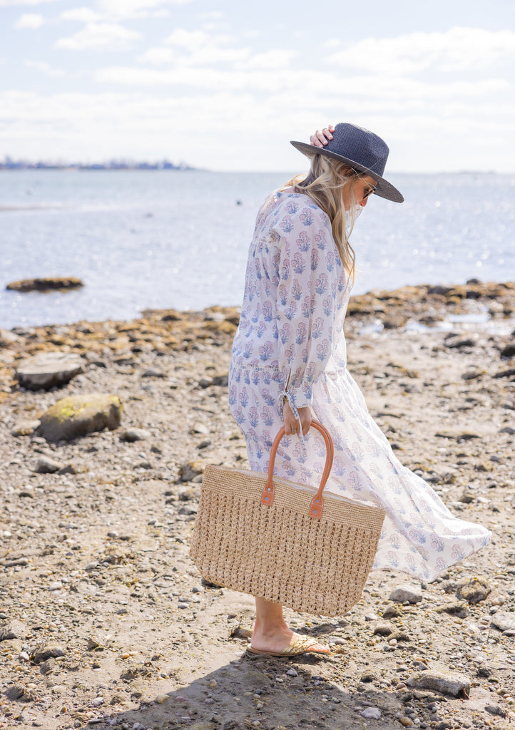 Vented Sun Hat in black on model walking on the beach with a straw beach bag and white floral dress