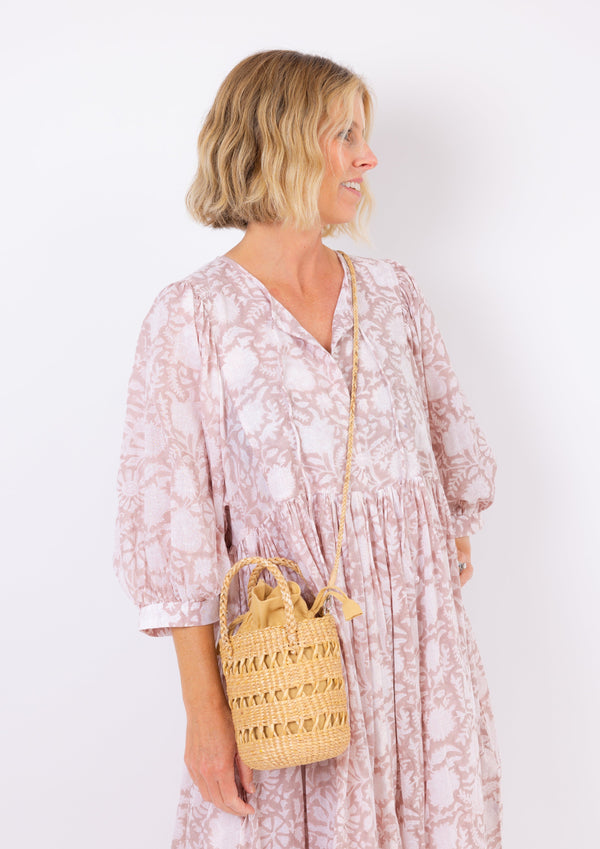 Open weave mini water hyacinth bah with drawstring closure and crossbody strap on model in tan kaftan