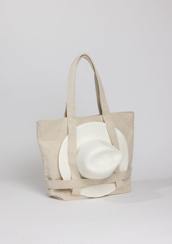 3/4 angle of a Natural colored canvas bag holding a hat with attached straps