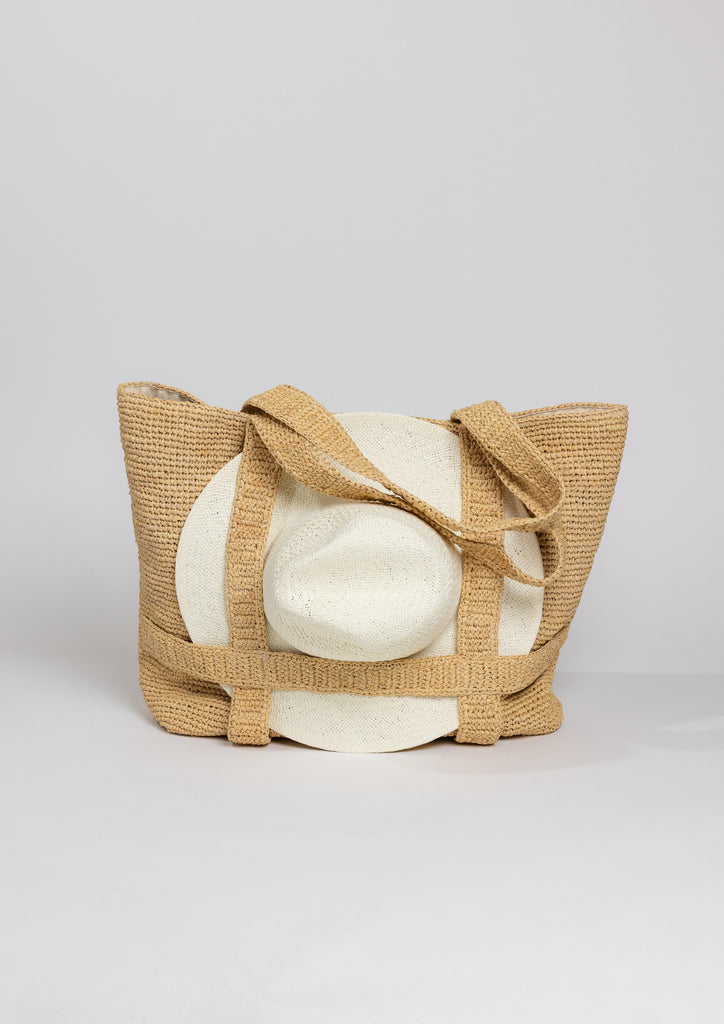 Straw bag with straps holding a white sunhat