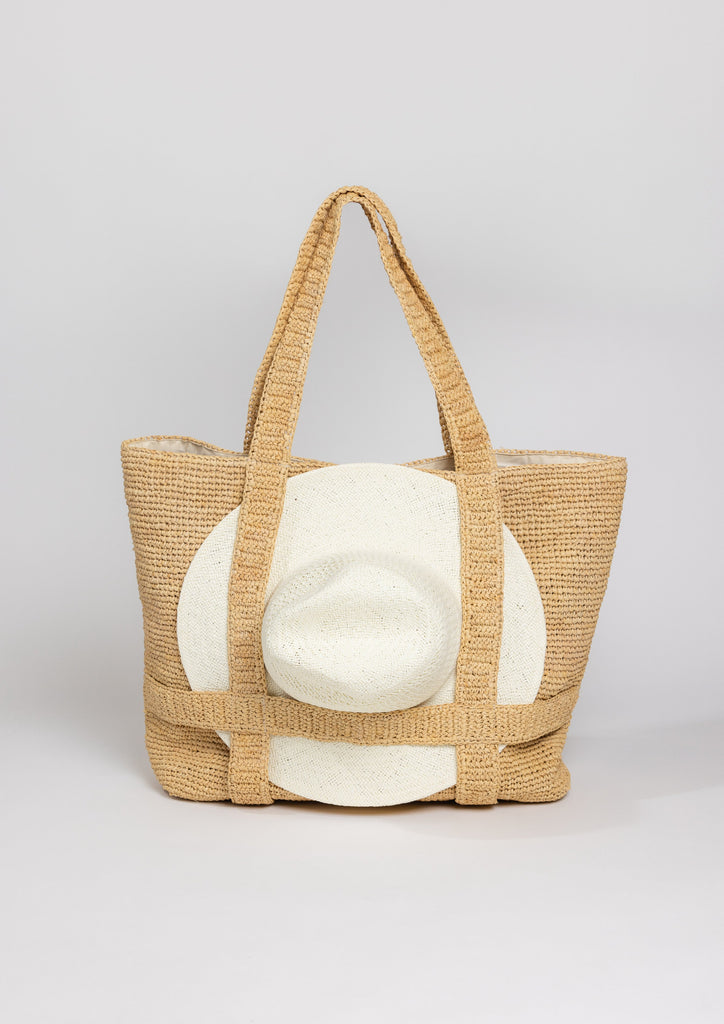 Straw bag with straps holding a sun hat with handle drop standing up