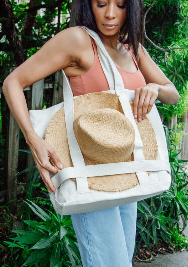 Model holding tan canvas bag with brimmed sun hat attached