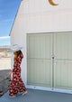 Model wearing red floral dress and white perforated hat in desert
