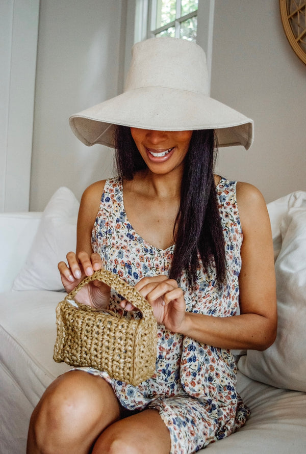 Tan packable hat on model holding mini straw bag
