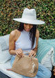 Model wearing white perforated sun hat and holding small tan bag