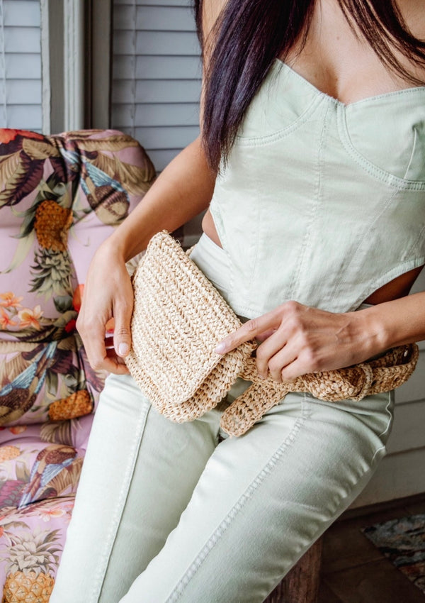 Model sitting and wearing straw belt bag at waist