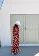 Model in red floral dress and white perforated sun hat in front of tan doors