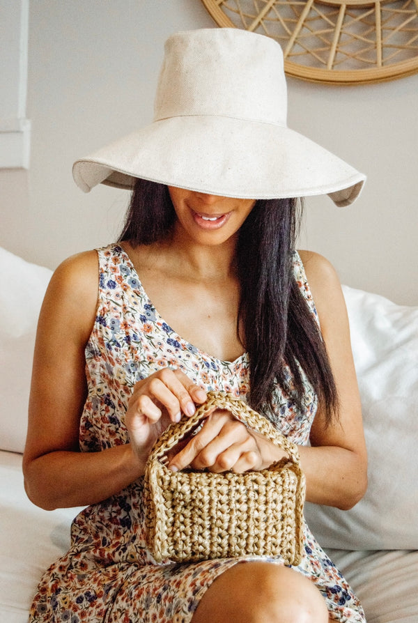 Model holding mini straw bag and wearing tan canvas sun hat