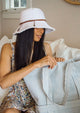Model wearing white fringe cotton bucket hat opening striped bag