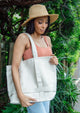 Model looking down wearing a sun hat and holding a tan canvas tote bag over her shoulder